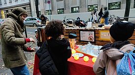 Eine Organisatorin schenkt am Stand vor dem Quartiersbüro zwei Kindern alkoholfreien Punsch aus.