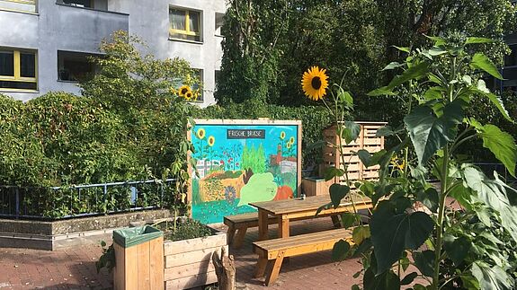 Blumen und Pflanzen blühen rund um eine Tafel und einen großen Tisch im Gemeinschaftsgarten „Frische Briese“. 