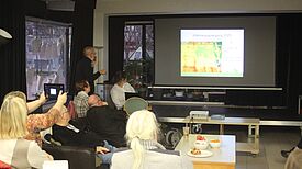 Auf einer Leinwand ist ein Foto der Wärmebildkamera zu sehen, davor sitzen Anwohnende.