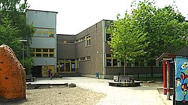 Der Schulhof der Grundschule am Amalienhof mit einem Spielplatz im Vordergrund und dem Schulgebäude im Hintergrund. 