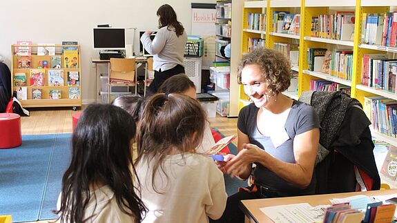 Leiterin Svenja Claussen spricht lächelnd mit einer Gruppe von Kindern in der Schulbibliothek der Eduard-Mörike-Schule.