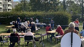 Anwohnende sitzen an Biertischen im Grünen und feiern die Wiedereröffnung des Rosengartens.